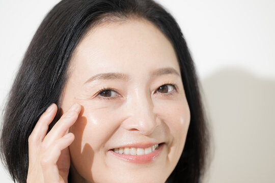 A middle-aged Japanese woman smiles while checking the wrinkles around her eyes: A closer look at anti-aging and skincare for women in their 50s