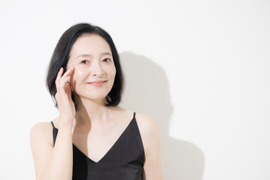 A middle-aged Japanese woman smiling as she touches her eyes; an anti-aging image of a woman in her 50s caring for wrinkles at the corners of her eyes and age-related skin concerns
