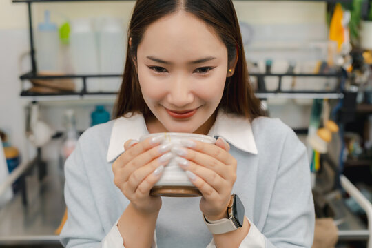 Matcha drink wellness concept. Smiling young woman enjoys the aroma of fresh green tea beverage in cafe kitchen, expressing relaxation and refreshment. matcha, drink, tea, cafe, wellness.