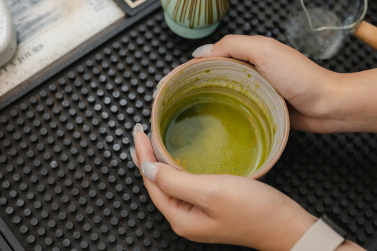 Matcha drink preparation concept. Hands holding ceramic cup of fresh green tea on a cafe counter, highlighting healthy beverage culture and wellness. matcha, drink, tea, cafe, healthy