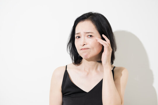 Middle-aged Japanese women concerned about wrinkles around their eyes and skin aging; women in their 50s who touch the corners of their eyes as if looking in a mirror, troubled by their appearance