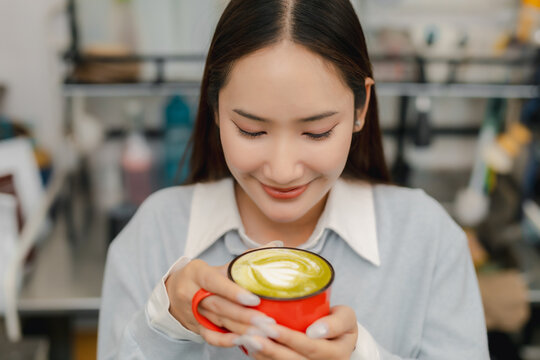 Matcha latte lifestyle concept. Smiling young woman holding fresh green tea latte with creamy foam in cafe, enjoying relaxing drink. matcha, latte, women, cafe, tea.