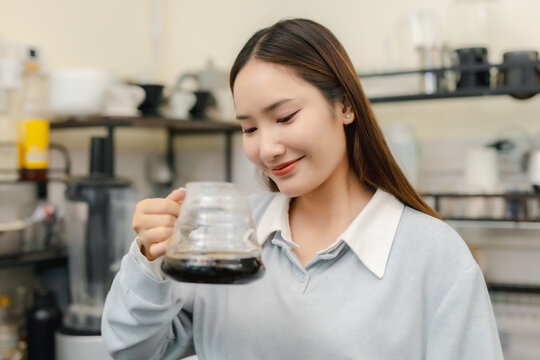 Smiling female barista holding glass server of freshly brewed pour over coffee at cafe, presenting handcrafted black coffee after manual brewing for professional beverage service.