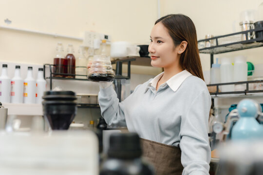 Smiling female barista holding glass server of freshly brewed pour over coffee at cafe, presenting handcrafted black coffee after manual brewing for professional beverage service.