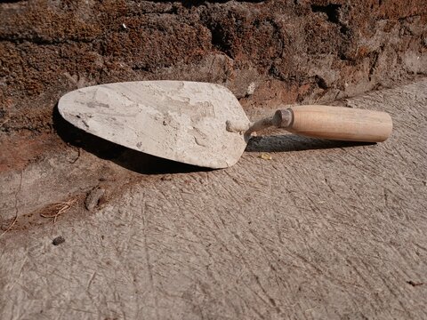 Used Masonry Trowel with Wooden Handle Leaning Against Brick Wall