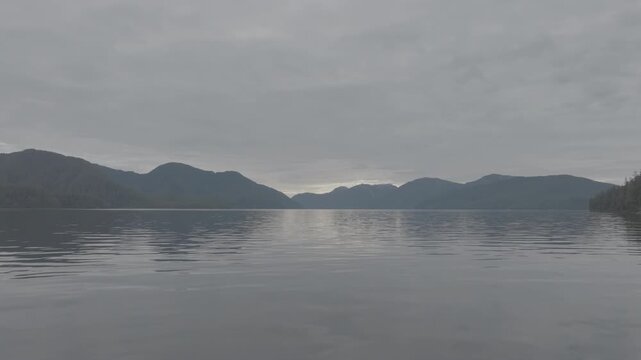 Aerial view of mirror calm water and layered mountain ridges in a coastal fjord at dawn &mdash; slow drift across still water