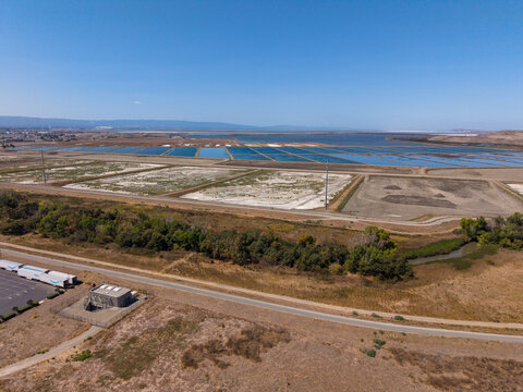 Industrial salt evaporation ponds and processing facilities stretch along the Milpitas coastline, aerial view of tidal wetlands, industry and nature under clear blue summer skies