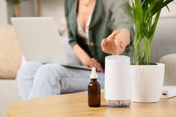 Fototapeta premium Wellness and self care at home, woman using essential oil diffuser and laptop for remote work and stress relief in a comfortable living room setting