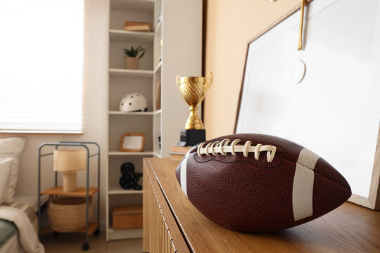 Achievement and sports success, american football ball and gold trophy cup on a wooden shelf in a bedroom with sports memorabilia and personal awards