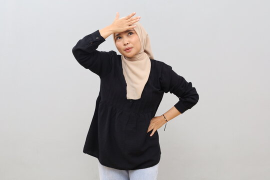 Portrait of young Asian woman in headscarf patting her forehead and looking up as a sign of forgetting something or making a mistake, standing on white background.