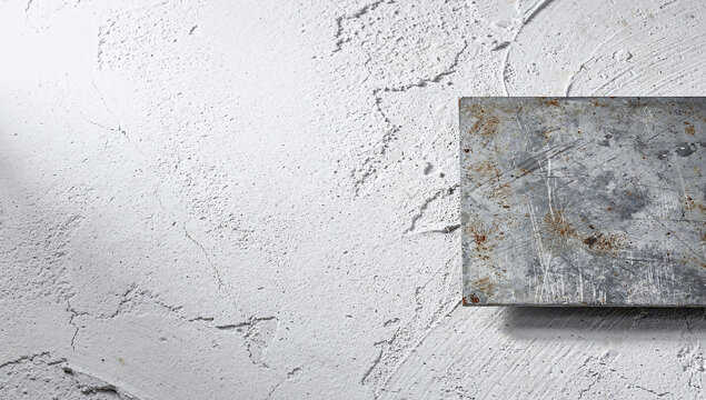 A scratched metal sheet with rust spots placed on a rough white textured plaster wall