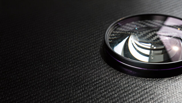 A camera lens filter resting on a black carbon fiber texture surface