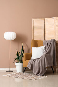 Armchair, lamp and folding screen near brown wall in room
