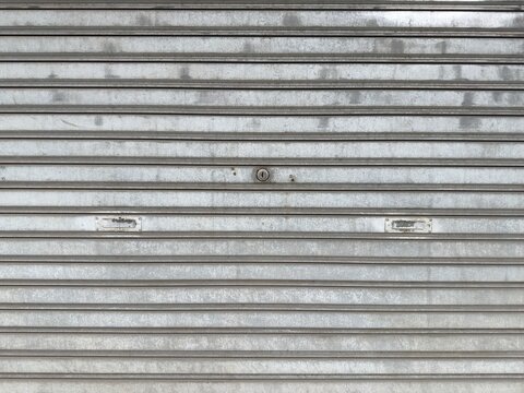 Closed metal rolling shutter door with keyhole and handles, industrial security gate texture background for architectural design use