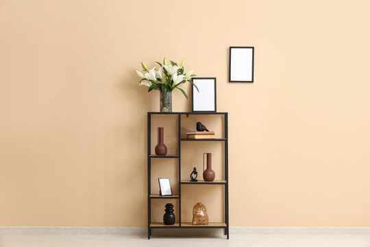 Shelving unit with vase of lily flowers and photo frames near beige wall in room