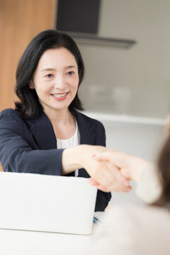 笑顔で握手をする日本人ミドル女性、商談や契約で相手と信頼関係を築く50代女性ビジネスパーソン