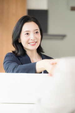 笑顔で握手をする日本人ミドル女性、商談や契約で相手と信頼関係を築く50代女性ビジネスパーソン縦