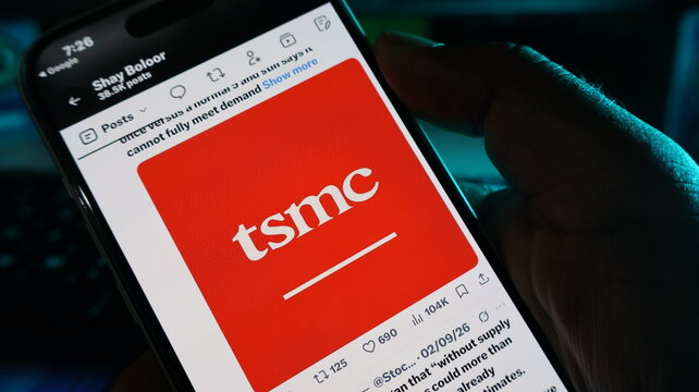 Mobile phone showing tsmc company logo on red background held by person against dark blurred technological setting. Kolkata, West Bengal, India, September 11, 2026
