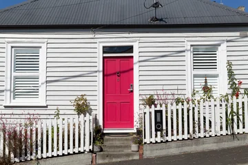 Weatherboard cottage painted grey with a bright red front door and a white picket fence © Steve Lovegrove