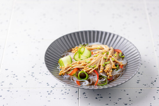 Glass noodles with cucumber, pepper and enoki mushrooms in a bowl on a gray background.