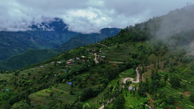 High angle drone shot of a switchback mountain road climbing a steep terraced hillside toward a fog-covered Himalayan peak