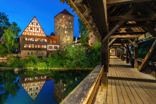 Beautiful evening blue hour view from inside the covered Henkersteg wooden bridge looking toward the illuminated historic Weinstadel and water tower in Nuremberg