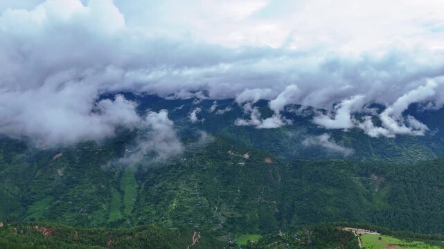 Aerial drone view of heavy low clouds rolling dramatically over steep green mountain peaks in the Nepalese Himalayas