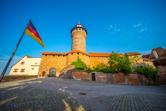 Scenic daytime view of the historic Imperial Castle (Kaiserburg) featuring the iconic Sinwell Tower and a waving German flag in Nuremberg