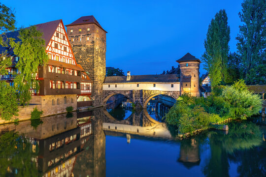 Beautiful evening blue hour view from inside the covered Henkersteg wooden bridge looking toward the illuminated historic Weinstadel and water tower in Nuremberg