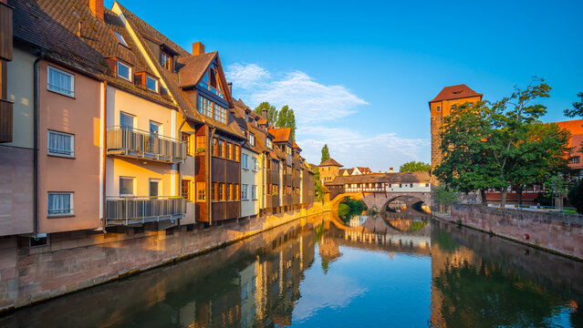 Scenic daytime view of the historic stone arch bridge spanning the calm waters of the Pegnitz River with beautiful architectural reflections in Nuremberg