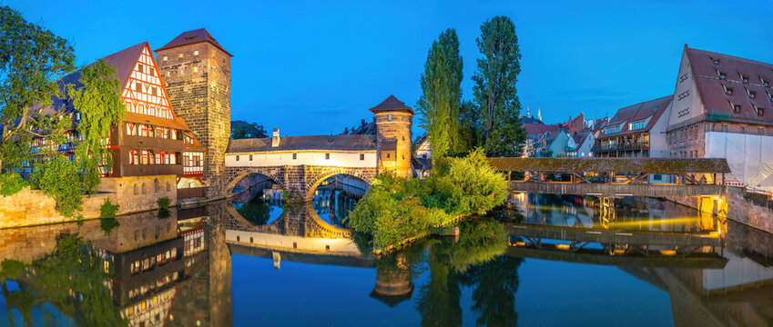 Beautiful evening blue hour view from inside the covered Henkersteg wooden bridge looking toward the illuminated historic Weinstadel and water tower in Nuremberg