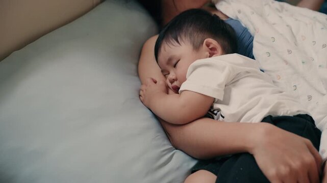 4K Video of Asian baby sleeping peacefully in mother's embrace on bed
