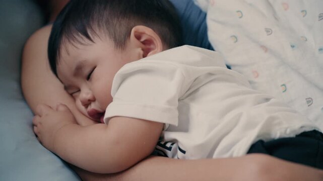 4K Video of Asian baby sleeping peacefully in mother's embrace on bed