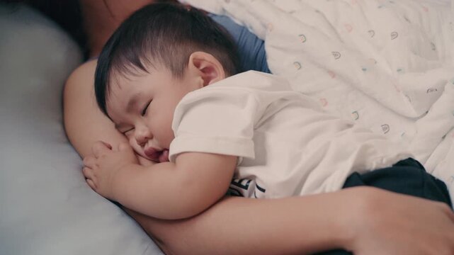 4K Video of Asian baby sleeping peacefully in mother's embrace on bed