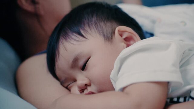 4K Video of Asian baby sleeping peacefully in mother's embrace on bed
