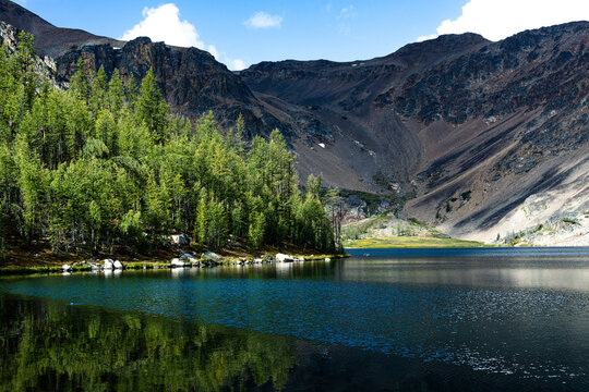 Alpine lake and green forest below a rugged mountain ridge