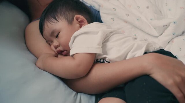 4K Video of Asian baby sleeping peacefully in mother's embrace on bed
