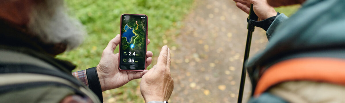 Caucasian senior men holding smartphone with navigation app while trekking in forest. Concept of outdoor activity, retirement lifestyle, suitable for eco tourism and mobile tech promo