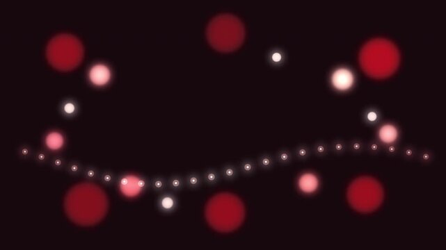 Wavy string of glowing festive red and white lights with bokeh effect on dark background, motion graphic