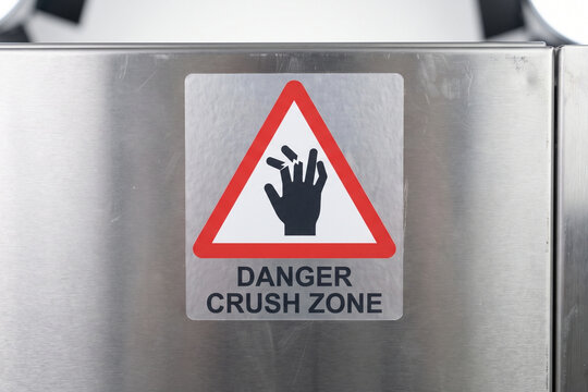Danger Crush Zone" industrial safety sign sticker with hand crushing pictogram warning symbol on a brushed stainless steel machinery surface.
