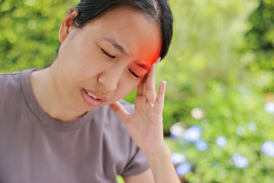 Unhappy Asian woman sitting on chair touching her head with red highlighted area indicating severe headache, migraine or brain pain. Concept of stress, sickness, healthcare, tension and mental health.