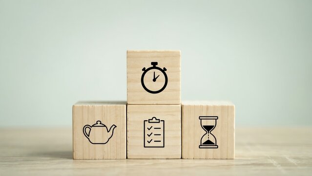 Wooden blocks with icon symbols including a stopwatch, teapot, checklist, and hourglass on a wooden table. Use for time management and productivity concepts.