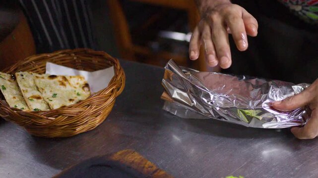 Chef Wrapping Fresh Naan Flatbread in Tin Foil for Takeaway