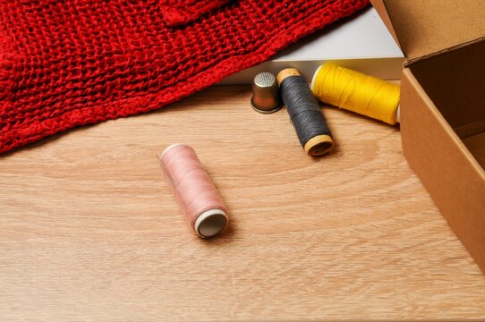 Sewing supplies including thread spools, thimble, and red fabric on a wooden table