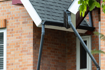 Black rain gutters drain water from a house roof © Rattanachat