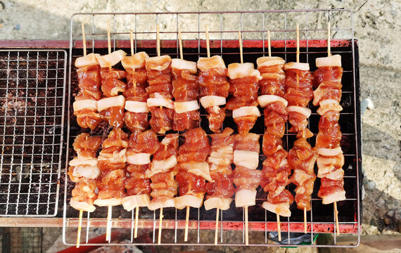 Raw Thai grilled pork skewers (Moo Ping) ready to cook on a barbecue grill.