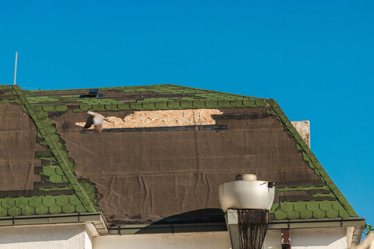 Damaged Green-Tiled Roof and Chimney Against Blue Sky
