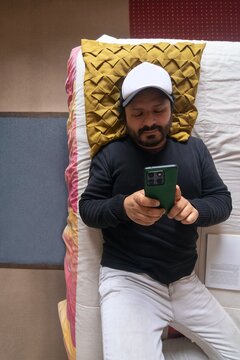 A top-down, vertical view of a man lying in bed, having a conversation via text message on his cell phone