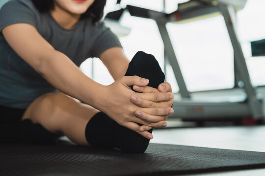 Close-up of woman stretching leg seated on exercise mat in gym preparing for workout or cool down routine