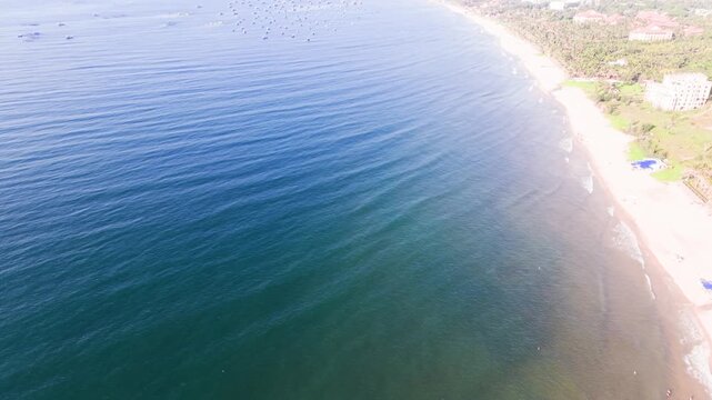View the clear waters and blue skies in Xuan Thuy, Mui Ne, Lam Dong. This region features a long beach with gentle waves. People enjoy various activities along the shore, creating a lively atmosphere.